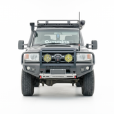 A front-facing view of a black off-road Toyota Land Cruiser with a heavy-duty front bumper, dual round auxiliary lights, a roof rack, isolated on a white background.