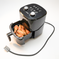 A black air fryer with its drawer pulled open, showing cooked chicken wings inside, on a clean white background with its power cord visible.
