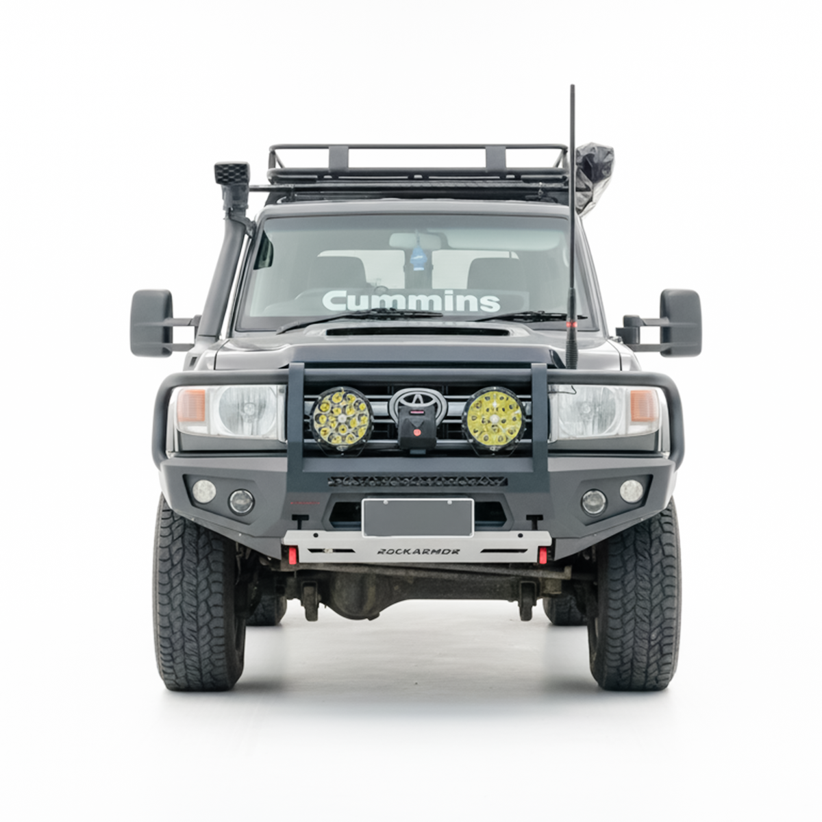 A front-facing view of a black off-road Toyota Land Cruiser with a heavy-duty front bumper, dual round auxiliary lights, a roof rack, isolated on a white background.