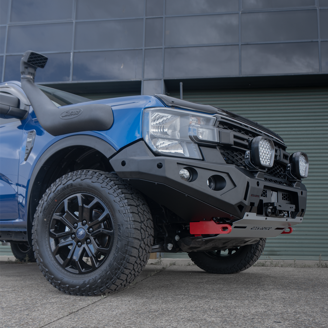 Blue Ford Ranger bakkie pickup truck with off-road modifications and Rockarmor bumper bull bar, photographed at a low angle in front of a building