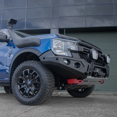 Blue Ford Ranger bakkie pickup truck with off-road modifications and Rockarmor bumper bull bar, photographed at a low angle in front of a building