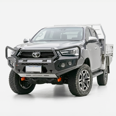 A dark gray Toyota Hilux bakkie pickup truck fitted with a heavy-duty Rockarmor black front bull bar and a silver metal flatbed carrier, photographed on a seamless white studio background.