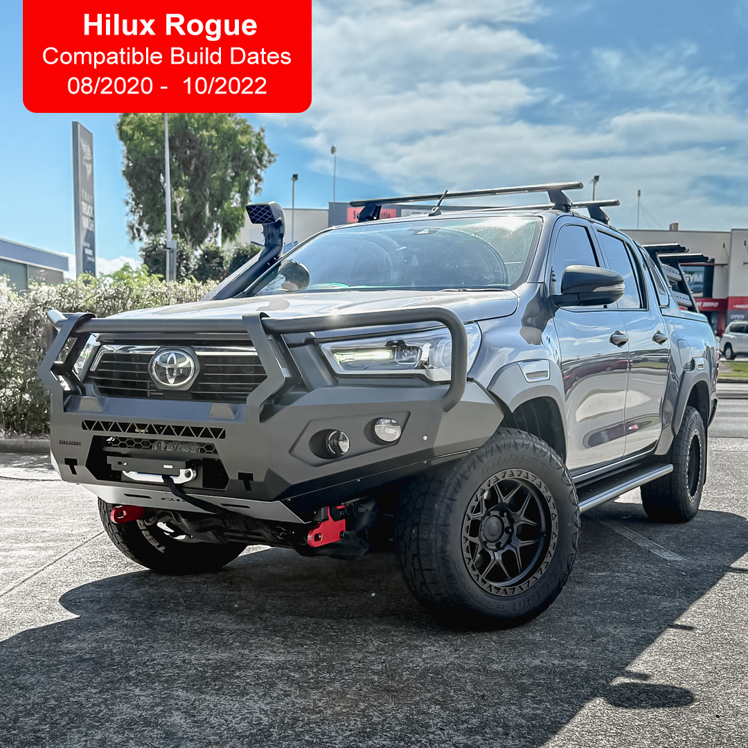 A silver Toyota Hilux pickup truck bakkie parked outdoors on a paved lot, shown from a front three-quarter angle. The truck is equipped with a black front bull bar manufactured by Rockarmor, off-road tires, roof racks, and a snorkel.