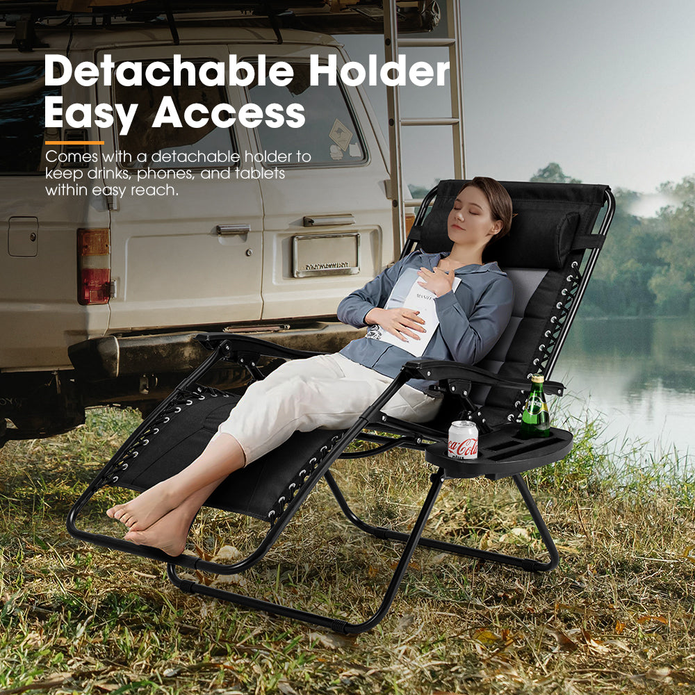 Person relaxing in a black lounge chair with a detachable holder near a vehicle by a lake.