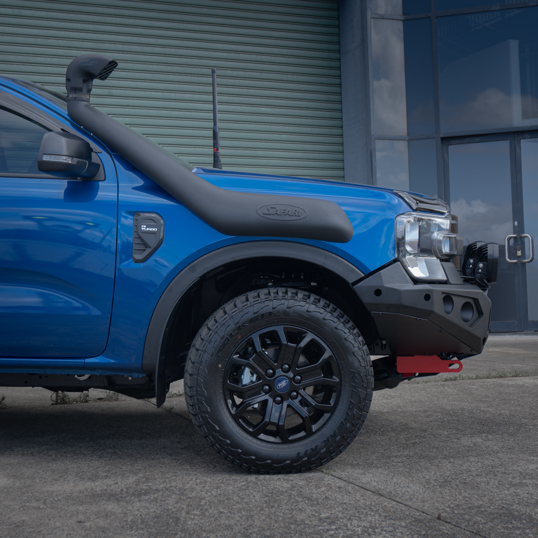 A blue Ford Ranger pickup truck bakkie shown from the side-front angle, parked outdoors in front of a building. The truck is equipped with a black snorkel, black fender and wheel arches, black wheels, and a black Rockarmor front bumper bull bar.