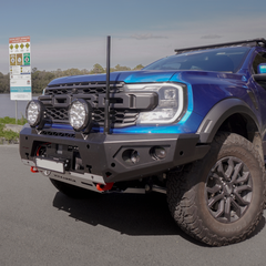 Blue off-road vehicle with large grille, Rockarmor bumper bul bar and additional lights on a road.