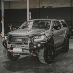A Ford Ranger pickup truck bakkie with a Rockarmor black front bumper bull bar, off-road tires, and a gray cap, photographed in a garage setting.