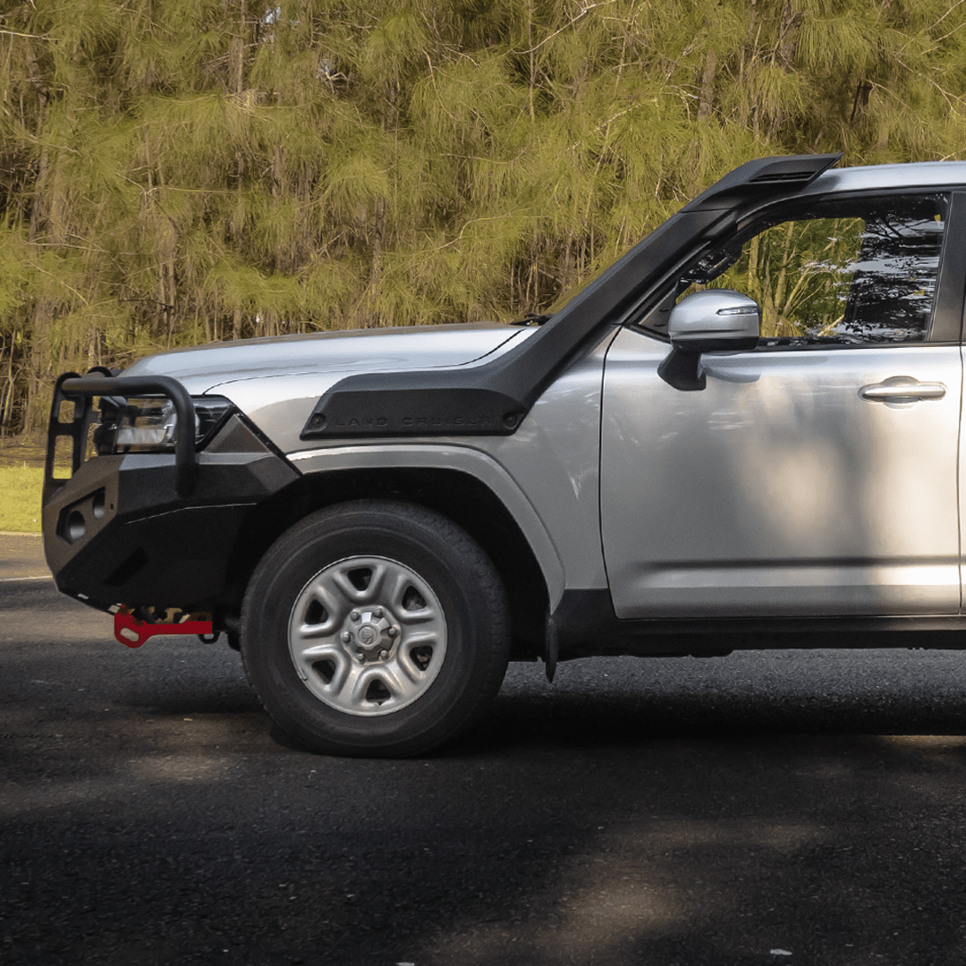 Silver SUV with black off-road bumper on a road with trees in the background