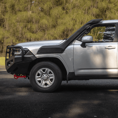 Silver SUV with black off-road bumper on a road with trees in the background