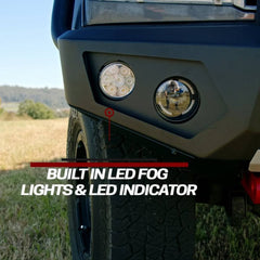 Close-up of the front bumper and wheel area of an off-road vehicle outdoors, showing two round built-in LED fog lights and a circular LED indicator. White text overlay reads 'BUILT IN LED FOG LIGHTS & LED INDICATOR'.