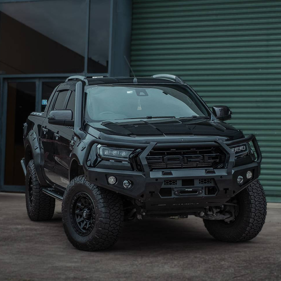 A black lifted Ford Ranger pickup truck bakkie with a heavy-duty front bumper bull bar and off-road tires, parked in front of a green corrugated metal building. The Rockarmor brand is displayed at the bottom of the image.