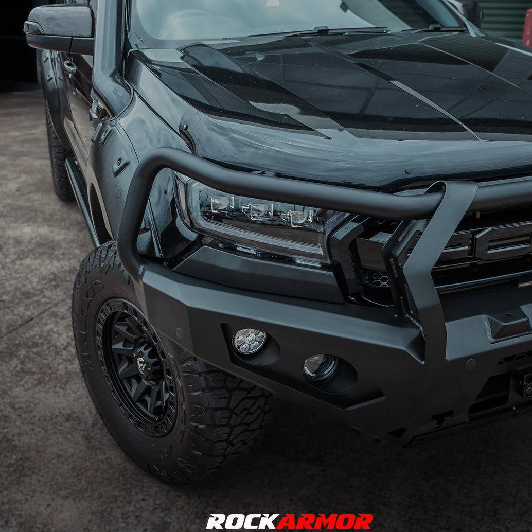 A black heavy-duty front bumper and bull bar mounted on a black pickup truck, shown in a garage setting. The Rockarmor brand logo and phone number are displayed at the bottom of the image.