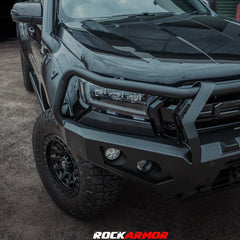 A black heavy-duty front bumper and bull bar mounted on a black pickup truck, shown in a garage setting. The Rockarmor brand logo and phone number are displayed at the bottom of the image.