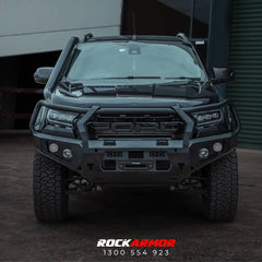 A black Ford Ranger pickup truck shown from the front, fitted with a heavy-duty Rockarmor front bumper and grille protector, parked outdoors in front of a garage or shed.