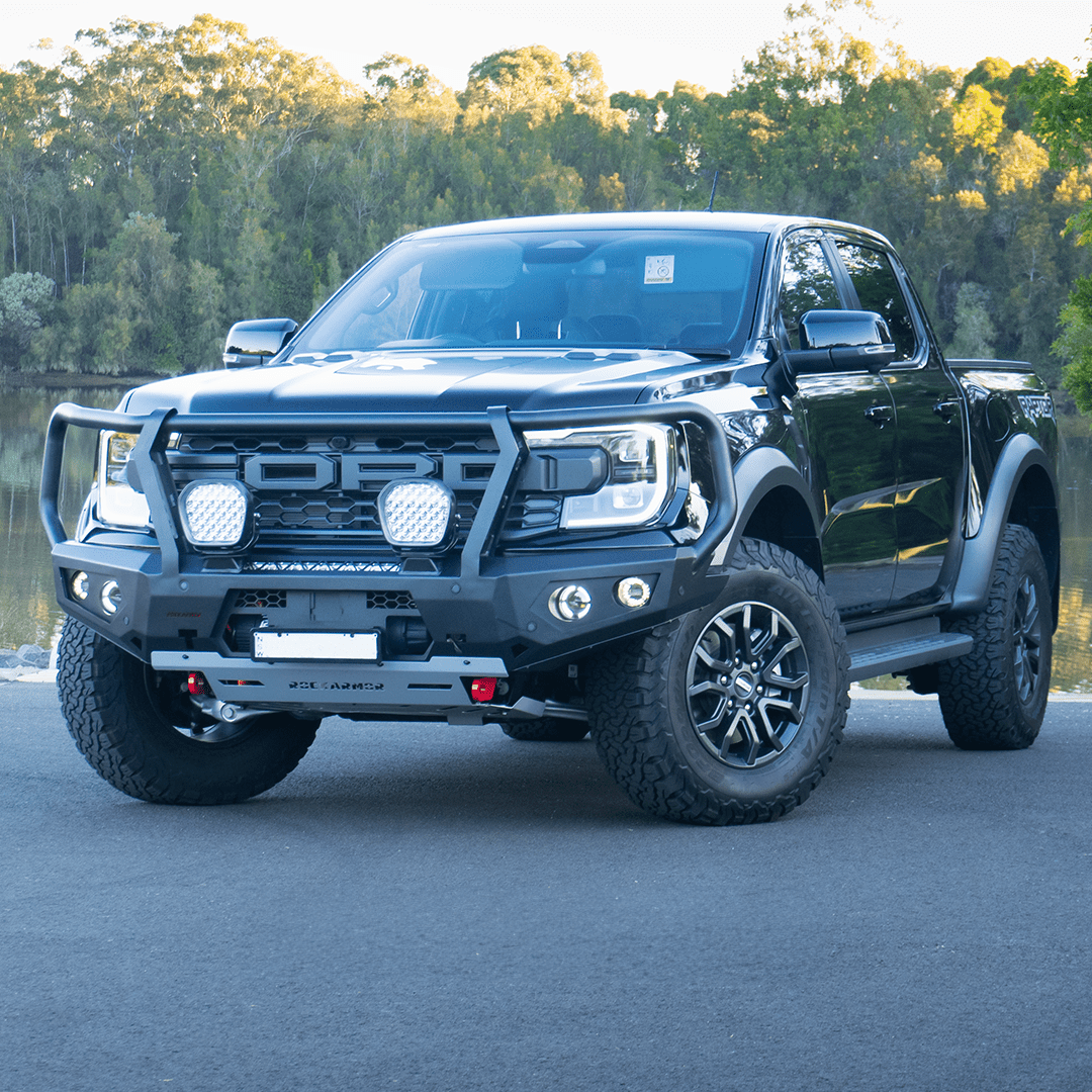 Gray Ford Ranger Raptor bakkie pickup truck with Rockarmor front bumper bull bar parked outside on a road near a body of water.