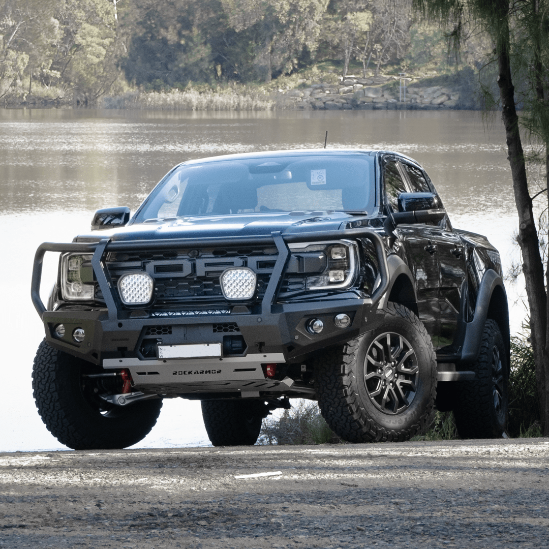 Gray Ford Ranger Raptor bakkie pickup truck with Rockarmor front bumper bull bar parked near a body of water.