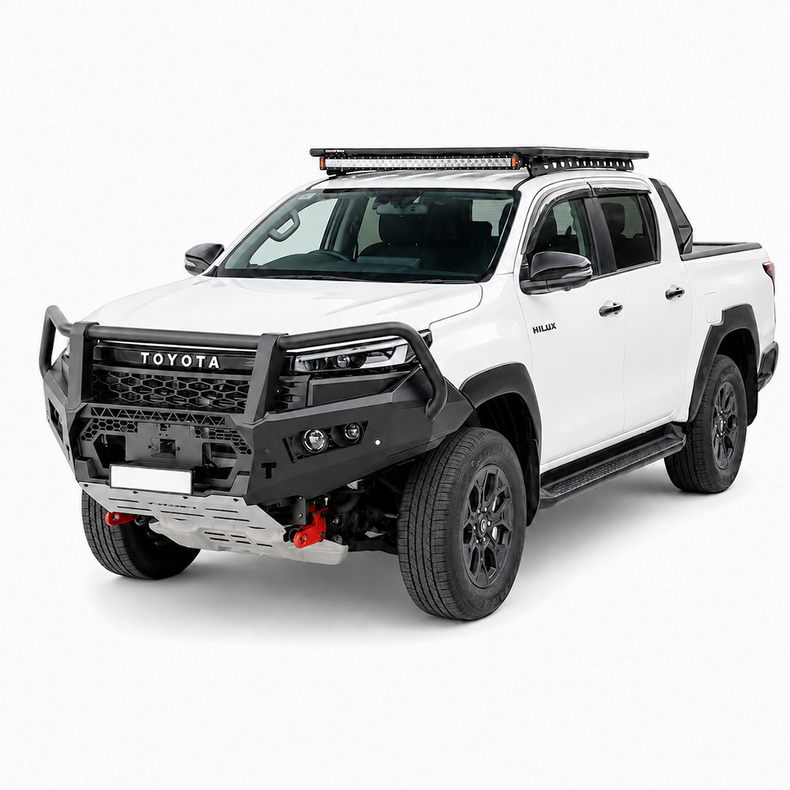 A front-facing studio shot of a white Toyota Hilux pickup truck bakkie equipped with a heavy-duty black Rockarmor bull bar, silver front bumper, roof-mounted LED light bar, and off-road tires on a light gray background.