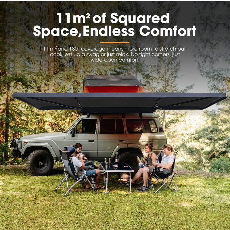 Family enjoying a picnic under a large vehicle-mounted awning in a forest setting.